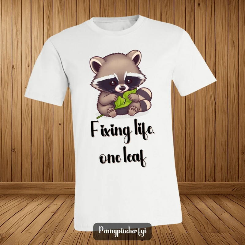 Funny t-shirt with a clever raccoon meticulously sewing a tiny tear in a leaf, showcasing its repair skills.
